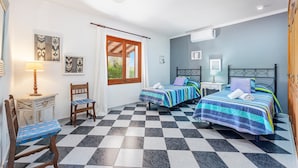 Ein Zimmer mit zwei Betten, einem Sessel, einem kleinen Tisch und einem Fenster mit Vorhängen.