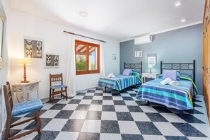 Ein Zimmer mit zwei Betten, einem Sessel, einem kleinen Tisch und einem Fenster mit Vorhängen.