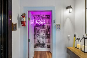 Un couloir avec une porte éclairée par un éclairage violet, un extincteur et un luminaire fixé au mur.