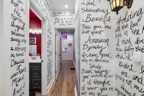 A hallway with a red wall and a white door, leading to a room with a chandelier. - Swiftie Suite on Music Row | 2BR 2BA | Sleeps 6 (Nashville)