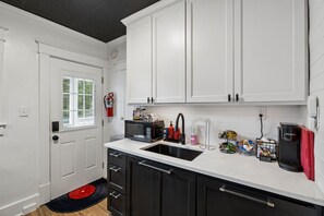 A compact kitchen with white cabinets, a black countertop, a microwave, a coffee maker, and a red rug. - Elvis`s Heartbreak Hotel on Music Row - Sleeps 6 (Nashville)
