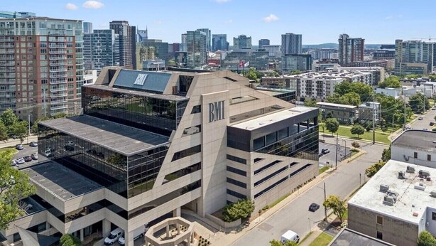 En modern byggnad med en framträdande skylt med texten ”BMI”, omgiven av en stadsbild med olika typer av byggnader.