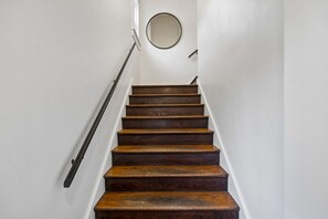 Eine Holztreppe mit Handlauf, weißen Wänden und einem runden Spiegel an der Wand.
