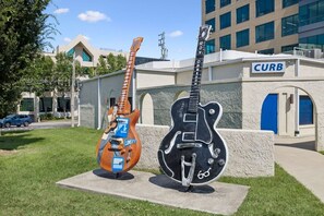 Zwei Gitarren auf Betonpodesten vor einem Gebäude mit einer blauen Tür und dem Schild 'CURB'.