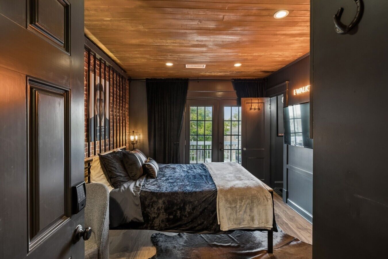 Une chambre à coucher avec un lit, une table de chevet, une lampe et une vue sur l’extérieur.