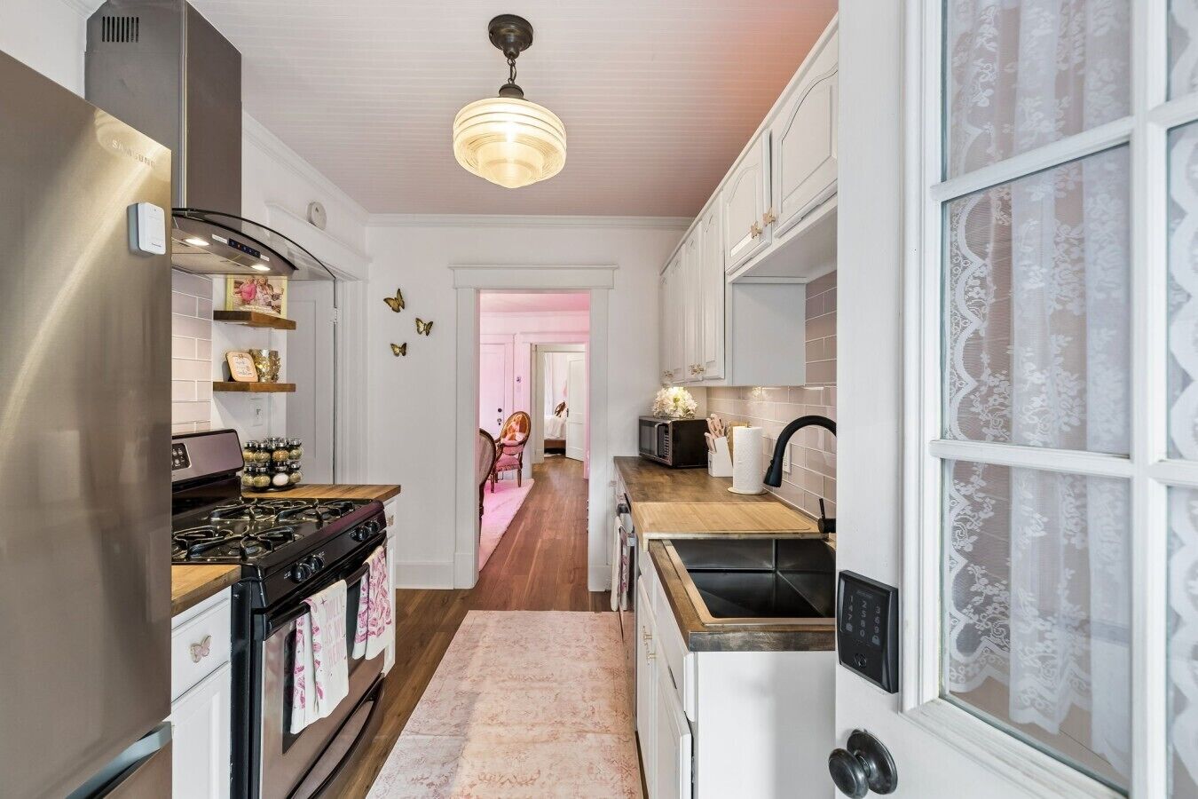 Une cuisine équipée d’une cuisinière, d’un four à micro-ondes et d’un réfrigérateur. On y trouve un plan de travail en bois et un tapis rose.