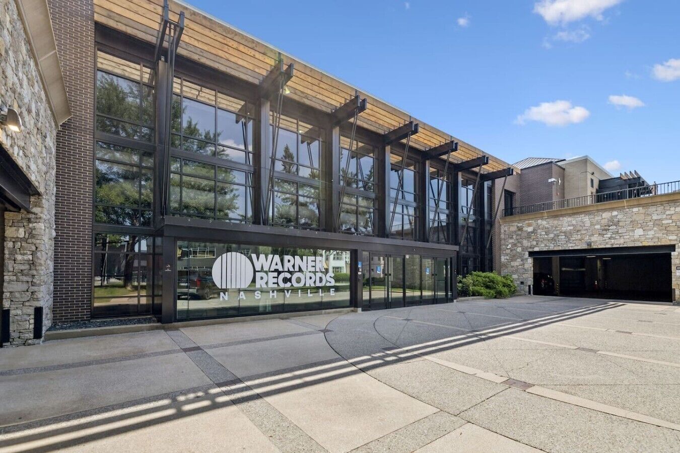 Un edificio con un amplio ventanal, un cartel de Warner Records Nashville y un estacionamiento.