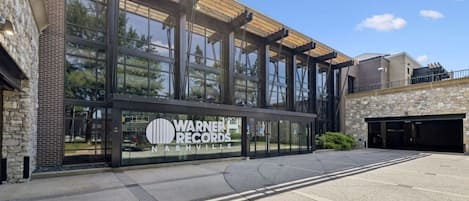 Un edificio con un amplio ventanal, un cartel de Warner Records Nashville y un estacionamiento.