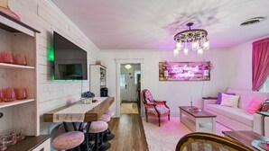 Una cucina moderna con angolo bar, un tavolo da pranzo con sgabelli e un soggiorno con divano e un elemento decorativo a parete.