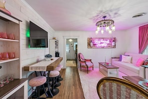 A modern kitchen with a bar area, a dining table with bar stools, and a living area with a sofa and a decorative wall piece. - Backwoods Barbie Suite | Sleeps 10 on Music Row (Nashville)