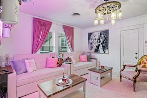 Een roze woonkamer met een bank, salontafel en een decoratieve fauteuil.