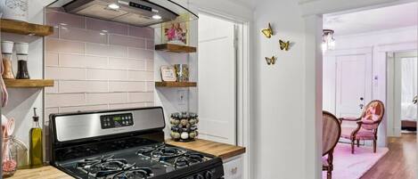 Una cocina moderna con estufa de acero inoxidable, encimeras de madera y salpicadero de azulejos blancos.