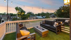 Una terrazza esterna con un braciere, sedute all'aperto e luci decorative a catena, con vista sulle case.