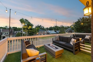 An outdoor deck with a fire pit, outdoor seating, and string lights against a backdrop of houses. - Backwoods Barbie Suite | Sleeps 10 on Music Row (Nashville)