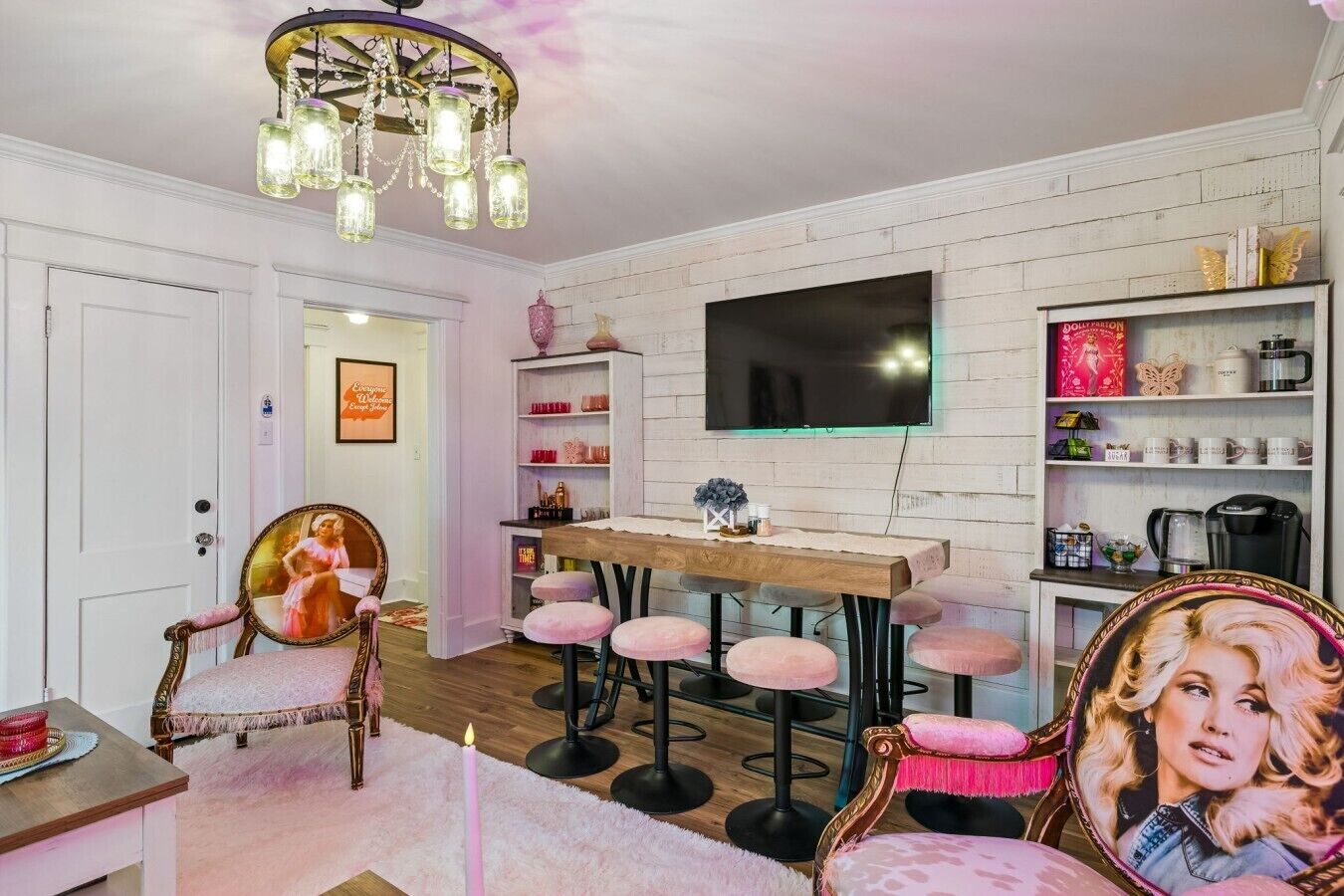 A room with a white brick wall, a flat-screen TV mounted above a wooden dining table, and a chandelier.