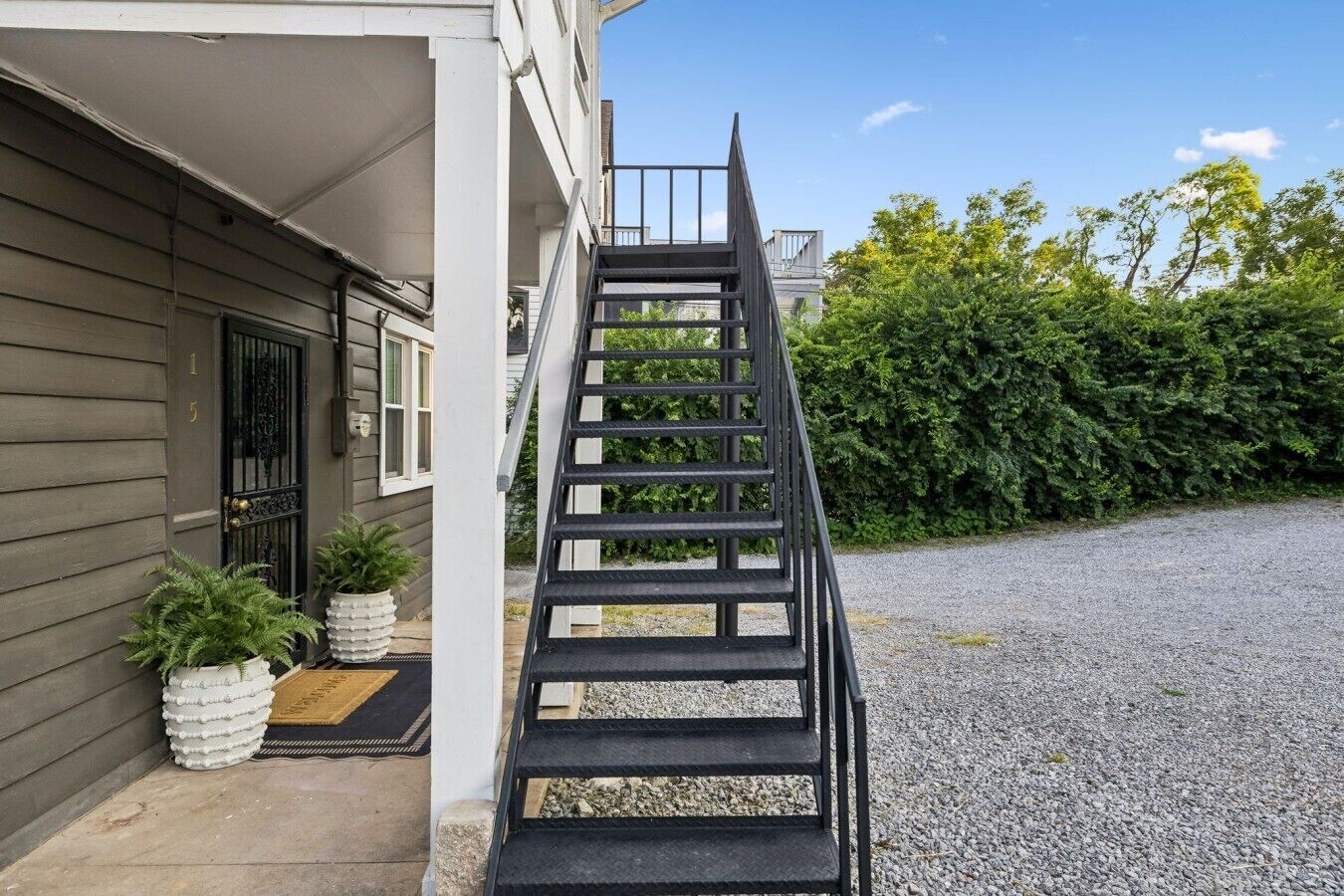Un immeuble résidentiel avec un escalier menant à l’entrée, une porte dotée d’un portail en métal et une allée gravillonnée.
