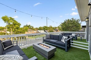 Um terraço no telhado com um conjunto de sofás cinza, uma lareira e luzes de cordão.