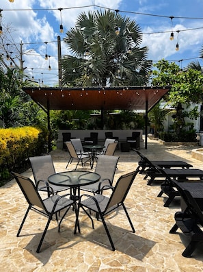 An outdoor patio with round tables and chairs, a covered seating area, and string lights.