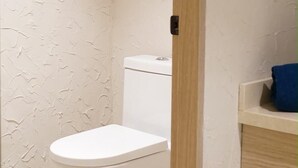 Un baño con inodoro, una puerta de madera y una toalla azul en un estante.