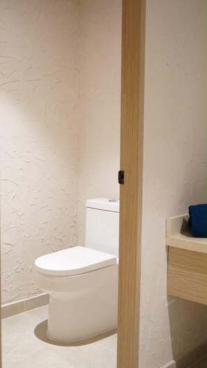 A bathroom with a toilet, a wooden door, and a blue towel on a shelf. - Manglea Luxury Hotel (Cartagena)