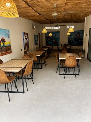 A restaurant interior with wooden tables and chairs, hanging pendant lights, and artwork on the walls.