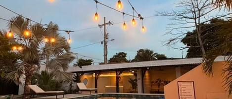 A poolside area with lounge chairs, a stone wall, and string lights.
