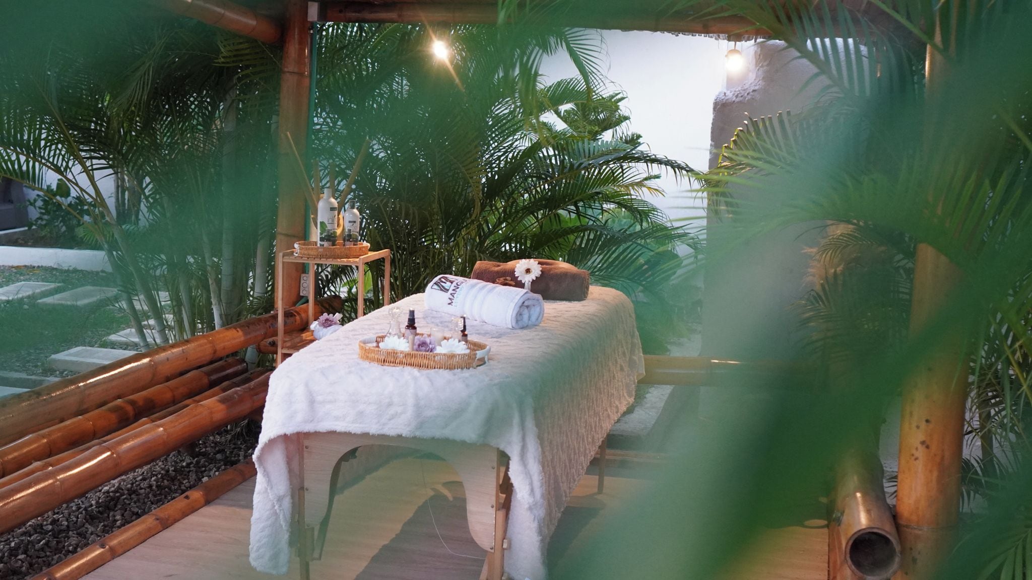 Zona de spa con una camilla de masaje, una toalla, una botella y una cesta.