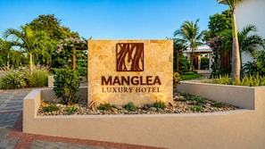 A sign for Manglea Luxury Hotel with a stone facade and a logo.