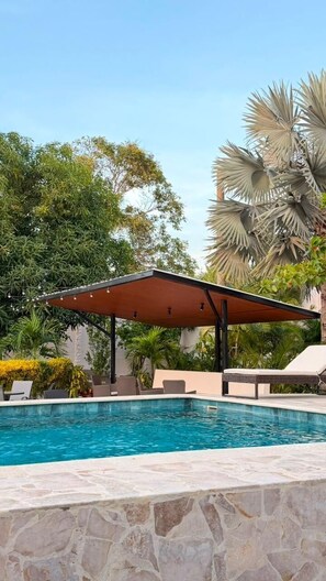 A swimming pool with a stone border, a covered seating area, and lush greenery in the background. - Manglea Luxury Hotel (Cartagena)