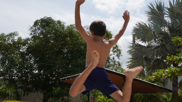 A person jumping into a swimming pool with a clear sky and trees in the background. - Manglea Luxury Hotel (Cartagena)