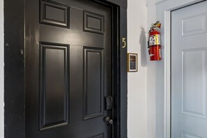 A black door with a number '5' on the wall beside it, a framed certificate, and a red fire extinguisher mounted on the wall. - Tennessee Whiskey Lounge on Music Row - sleeps 6 (Nashville)