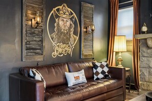 A leather sofa with patterned cushions, a wall-mounted clock, and a decorative wall piece with a name. - Tennessee Whiskey Lounge on Music Row - sleeps 6 (Nashville)