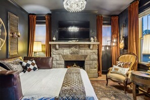 Un dormitorio con una cama grande, chimenea, televisor y candelabro.