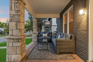 A covered porch with a stone column, a wicker sofa, and a small table. - Tennessee Whiskey Lounge on Music Row - sleeps 6 (Nashville)