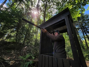 A person standing in a wooden structure with a metal roof, surrounded by a forested area. - Cozy stay at Haliburton Forest. Trails, Wolf Centre, Canopy Tour, 100 lakes! (Dysart and Others)