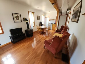 A living room with a TV, a fireplace, a dining table with chairs, and a kitchen area in the background.