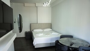 Quarto de hotel com cama, escrivaninha, cadeira, espelho e luminária na parede.