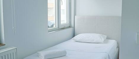 Habitación individual con cama, ventana, radiador y cabecera blanca.