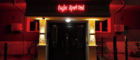 The entrance to a hotel with a neon sign, a gated entrance, and a tiled floor pattern.