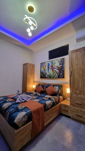 A bedroom with a bed, a wooden wardrobe, a painting of parrots, and a ceiling light fixture. - Villa Kupu-Kupu 2A – Romantic Lovina Sanctuary (Buleleng)