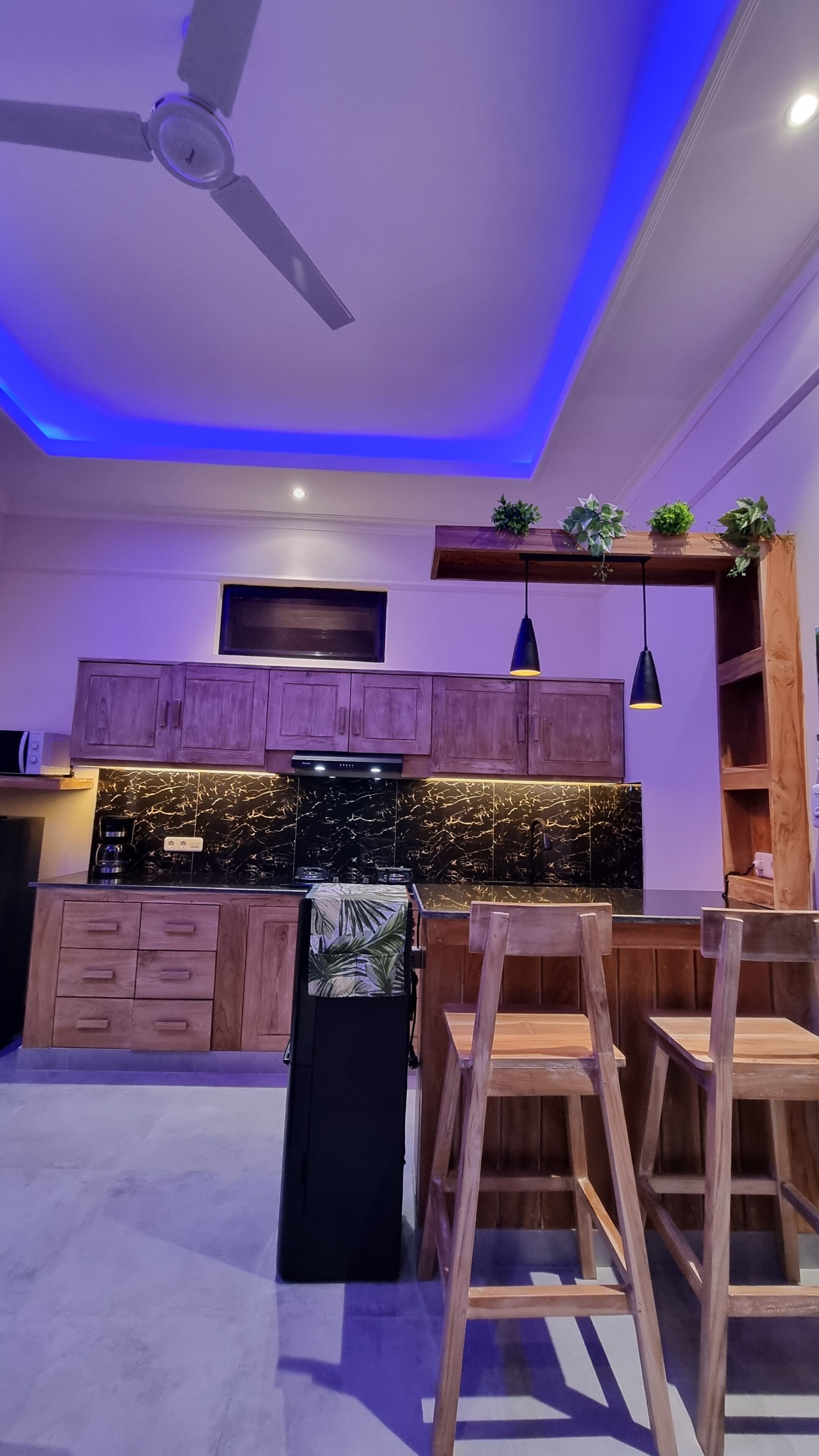 A modern kitchen with wooden cabinets, a black countertop, and a ceiling fan.
