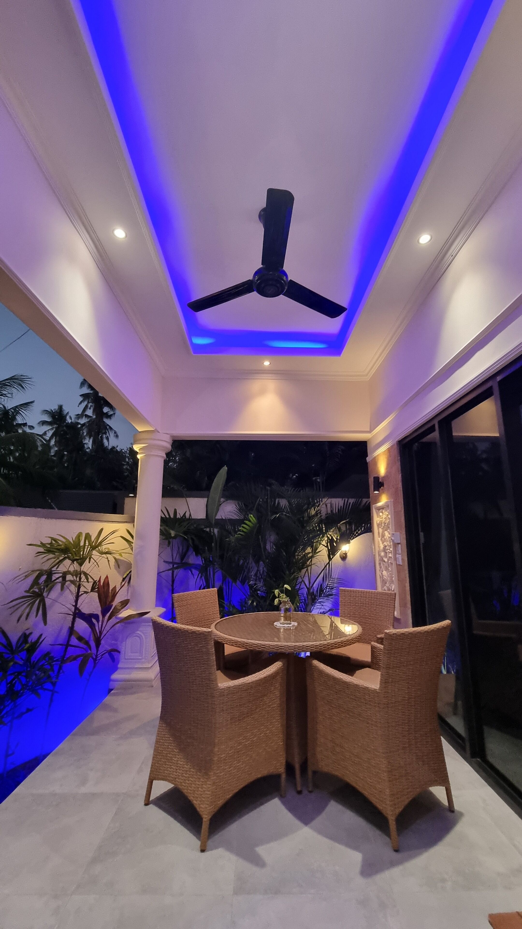 An outdoor patio with a ceiling fan, wicker furniture, and a glass table.