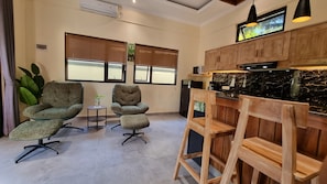 A modern interior with two upholstered chairs, a small table with a plant, a wooden bar area, and a television mounted above the bar. - "Romantic Lovina Sanctuary - Private Tropical Escape" (Buleleng)