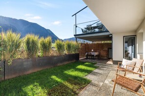 A modern outdoor patio with a dining area, a grassy lawn, and a view of mountains.