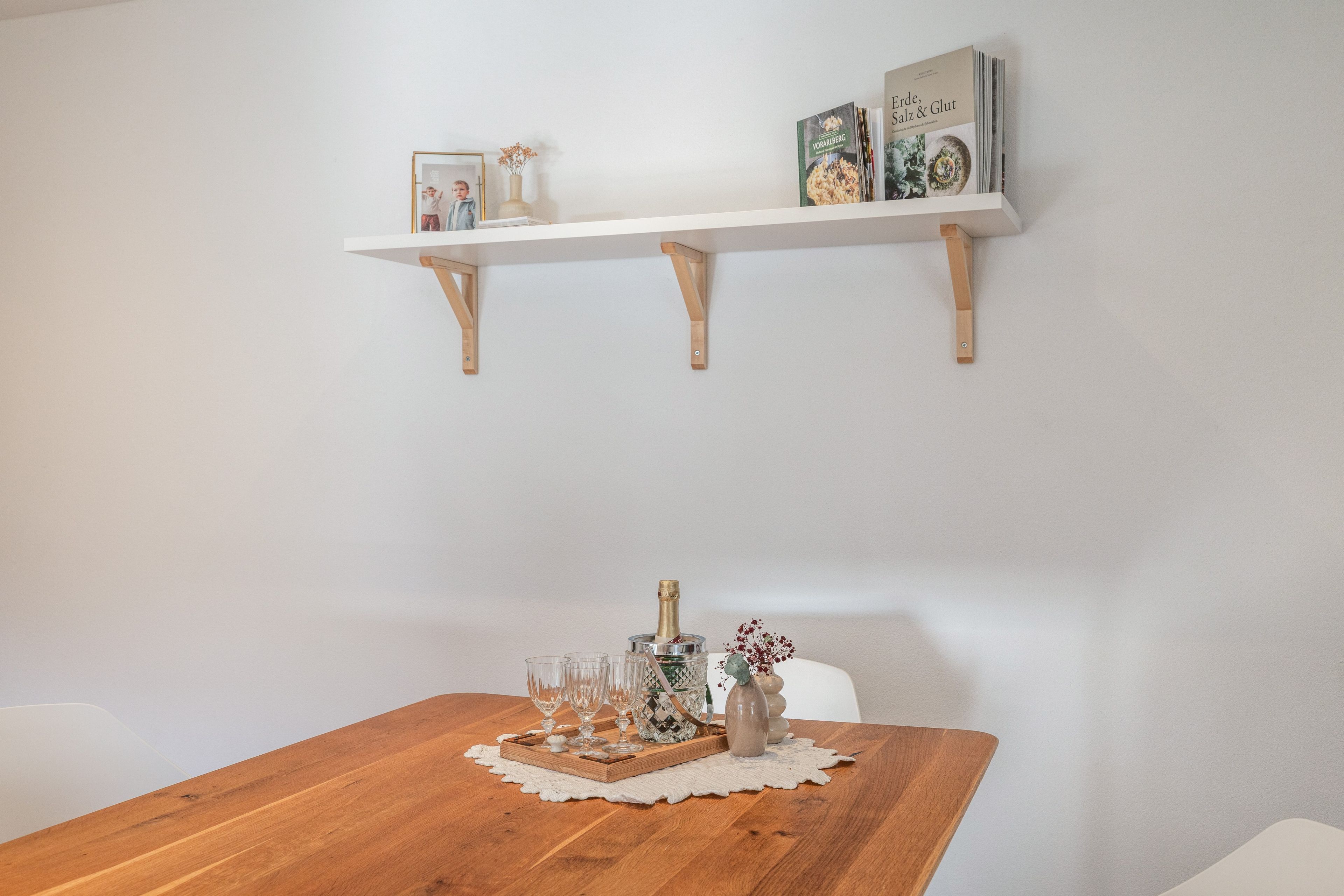 A dining table with a wooden finish, a white doily, a bottle of champagne, and several glasses.