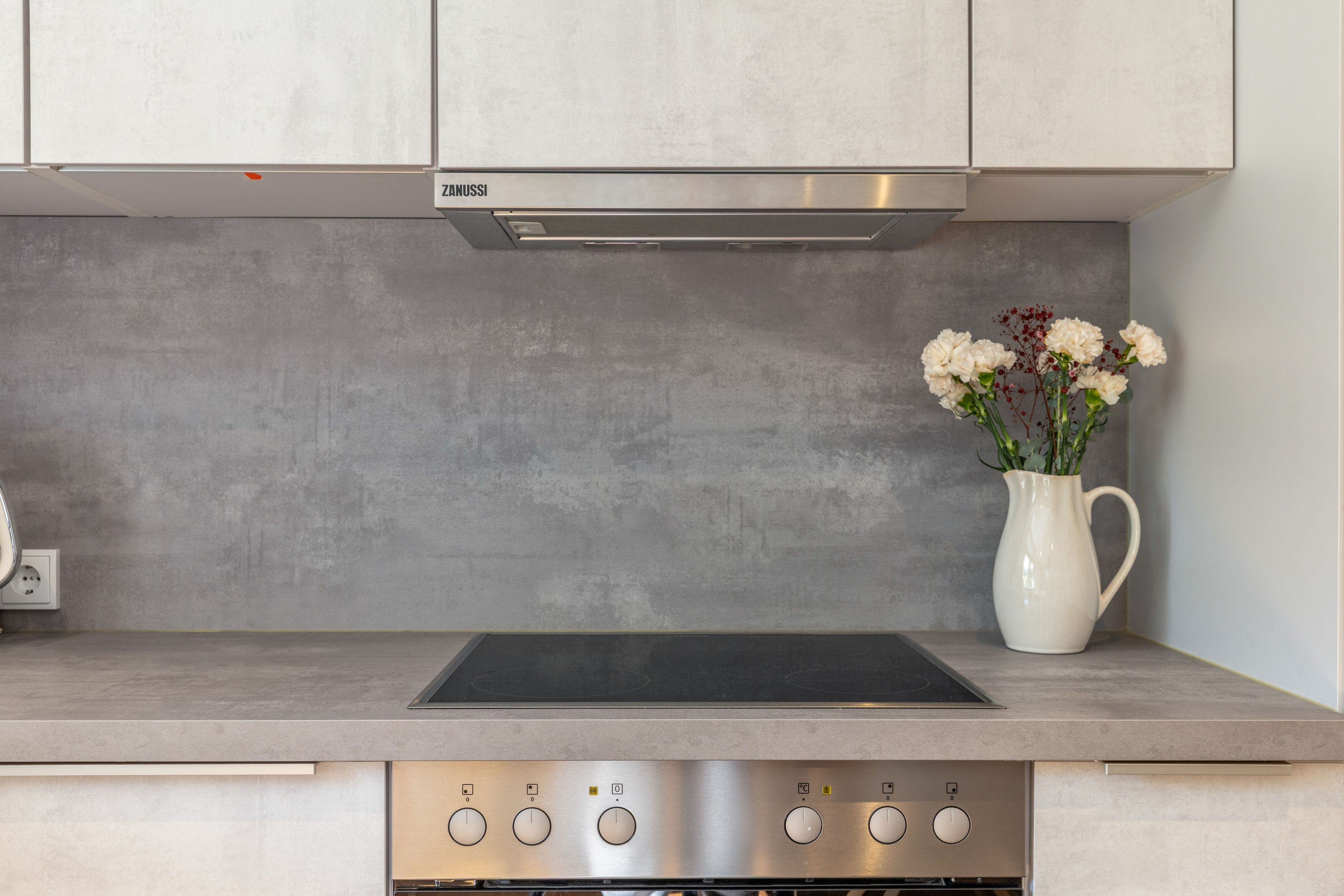 A kitchen with a stainless steel range hood, a built-in oven, and a white vase with flowers on the countertop.