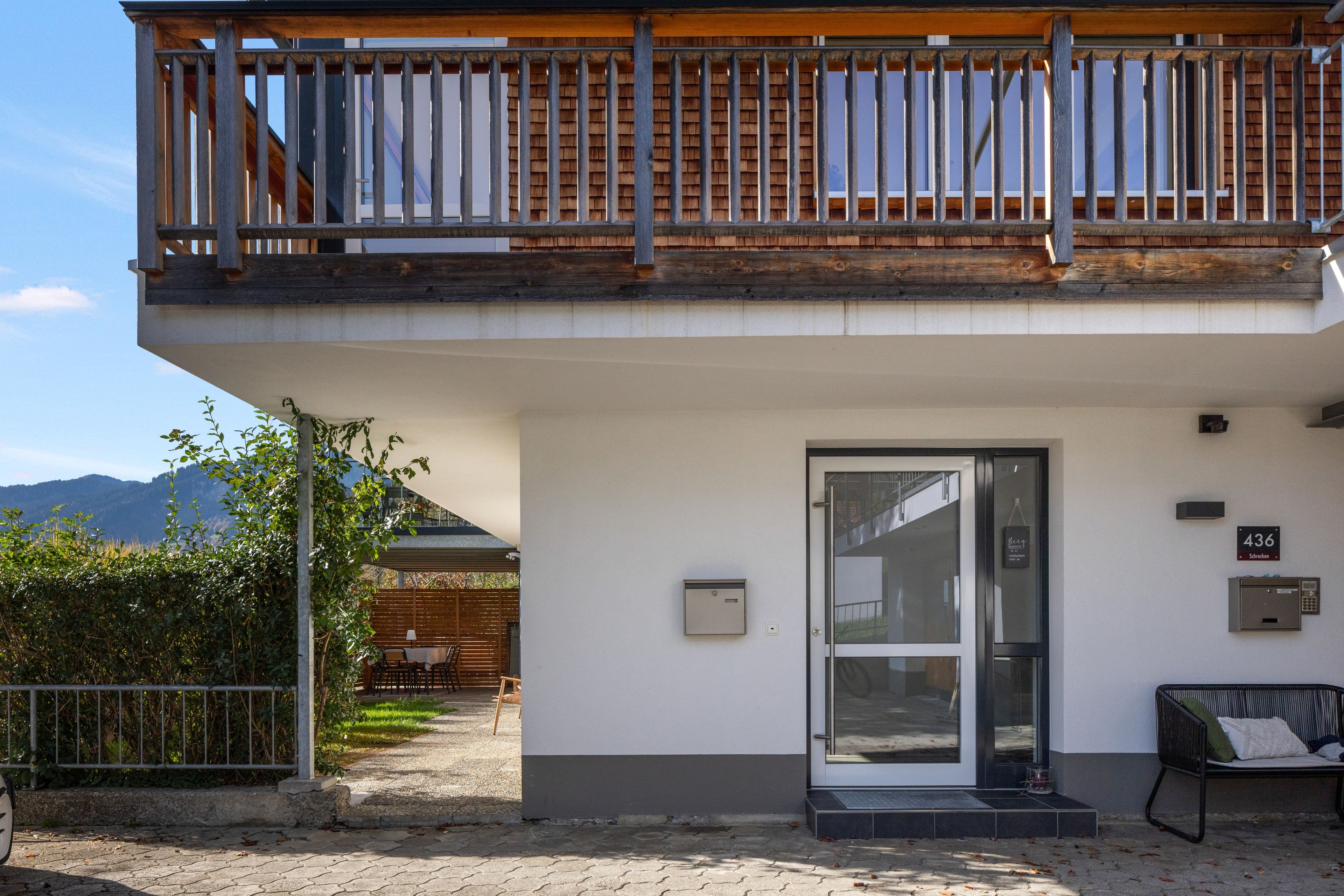 Un edificio moderno con un balcone, una porta con un pannello di vetro e una panchina all'esterno.