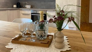 Una cocina moderna con una mesa de madera dispuesta para una celebración, con una botella de champán, copas y un florero con flores.