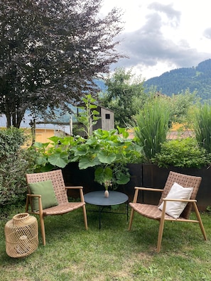 Un área de estar al aire libre con dos sillones de mimbre y una pequeña mesa redonda, rodeada de exuberante vegetación y vistas a la montaña.
