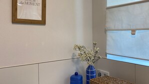 Un área de lavandería con una lavadora Siemens, una cita inspiradora enmarcada, un florero azul con flores y una cesta tejida sobre la lavadora.